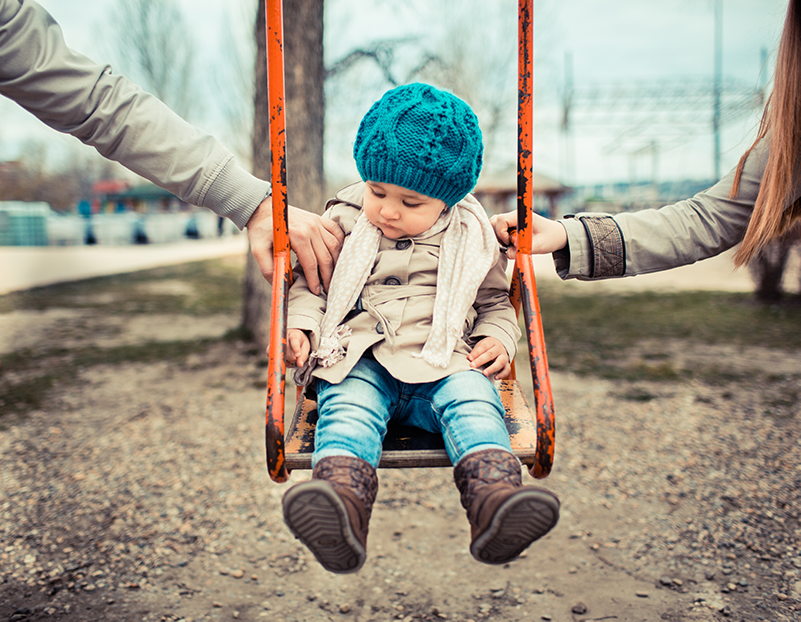 pieni lapsi kiikussa ja vanhemmat pitävät kiinni