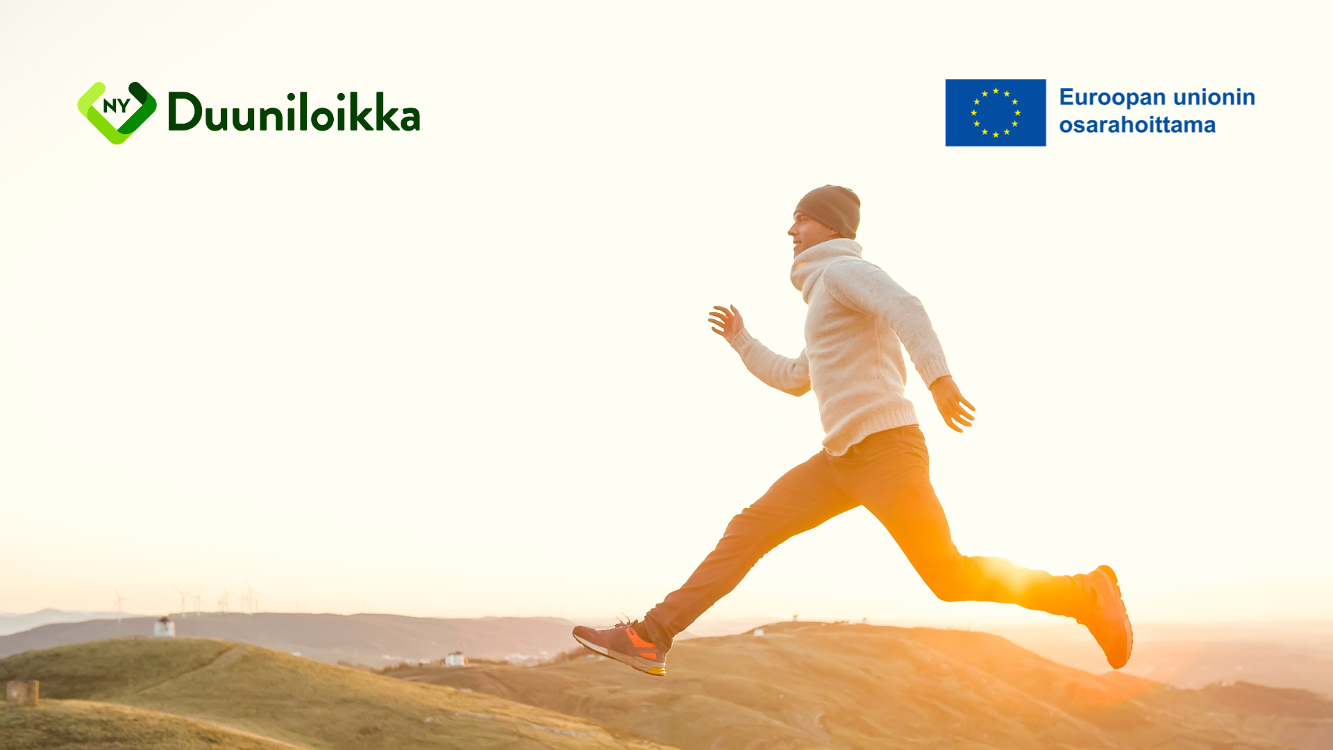 Mies loikkaa ilta-aurinkoisessa nummimaisemassa. Duuniloikka. Euroopan unionin osarahoittama.